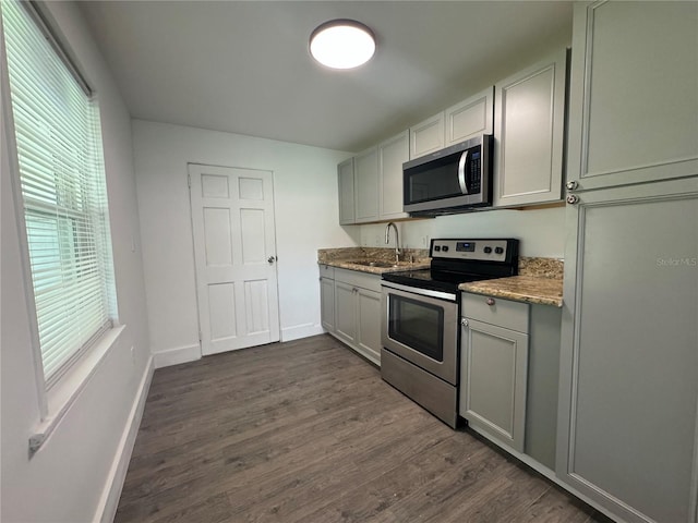 kitchen featuring appliances with stainless steel finishes, dark wood-type flooring, a sink, light stone countertops, and baseboards