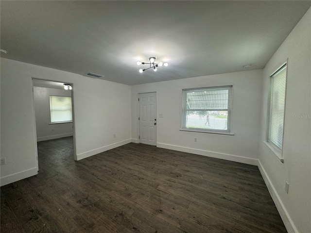 spare room with dark wood-style flooring, visible vents, and baseboards