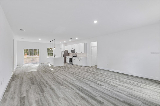 unfurnished living room with light wood finished floors, recessed lighting, visible vents, a sink, and baseboards