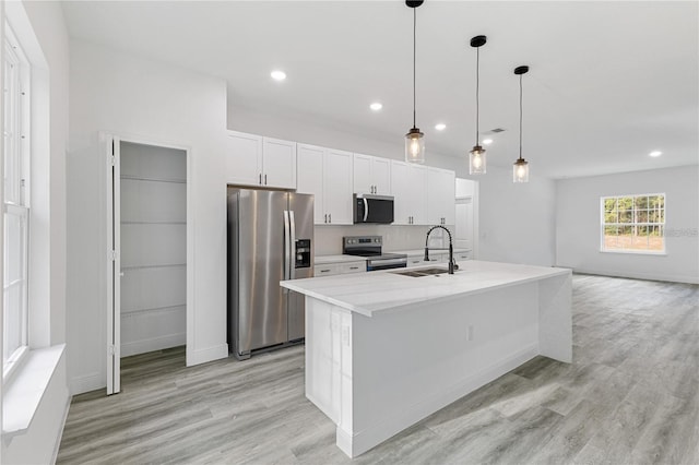 kitchen featuring appliances with stainless steel finishes, decorative light fixtures, a kitchen island with sink, white cabinetry, and a sink