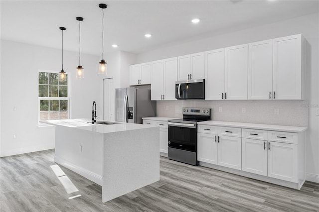 kitchen with pendant lighting, stainless steel appliances, light countertops, a kitchen island with sink, and a sink