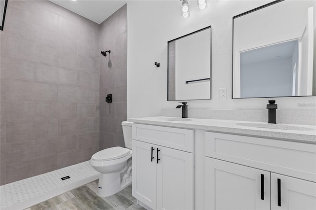 full bathroom with double vanity, toilet, a sink, a tile shower, and wood finished floors