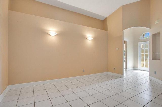 empty room featuring arched walkways, a towering ceiling, baseboards, and light tile patterned floors