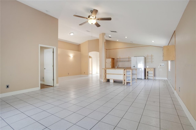 unfurnished living room featuring arched walkways, ceiling fan, light tile patterned floors, high vaulted ceiling, and baseboards