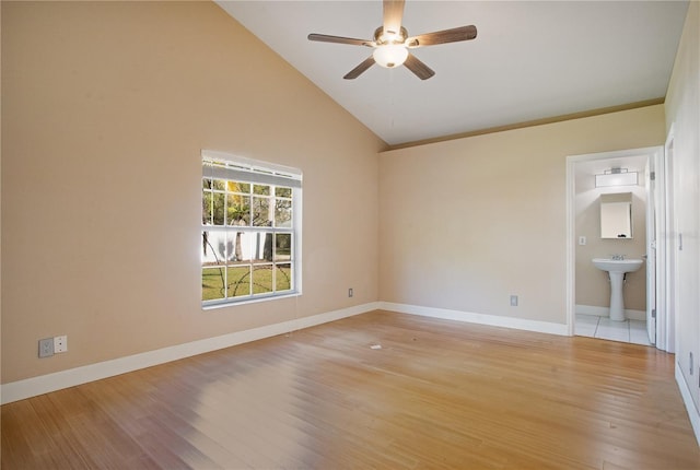 empty room with baseboards, light wood-style flooring, ceiling fan, high vaulted ceiling, and a sink