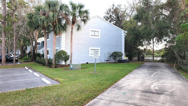 view of property exterior featuring central AC, uncovered parking, a lawn, and fence