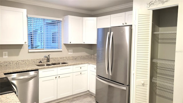 kitchen featuring light stone counters, a sink, white cabinets, ornamental molding, and appliances with stainless steel finishes