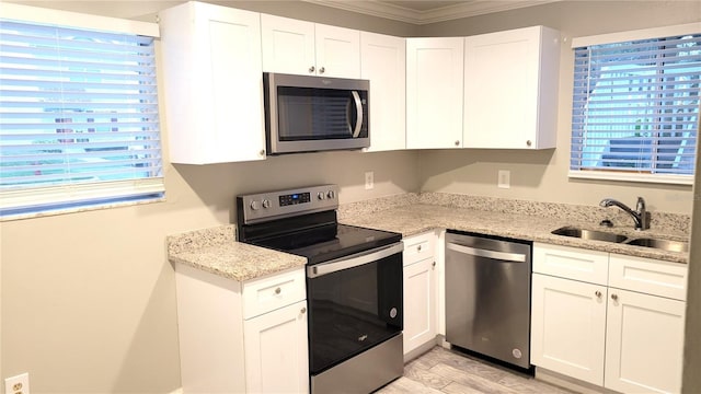 kitchen with stainless steel appliances, light stone counters, a sink, and white cabinetry