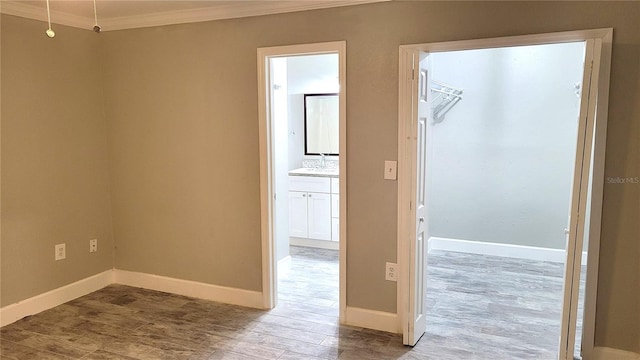 spare room featuring baseboards, crown molding, a sink, and light wood finished floors