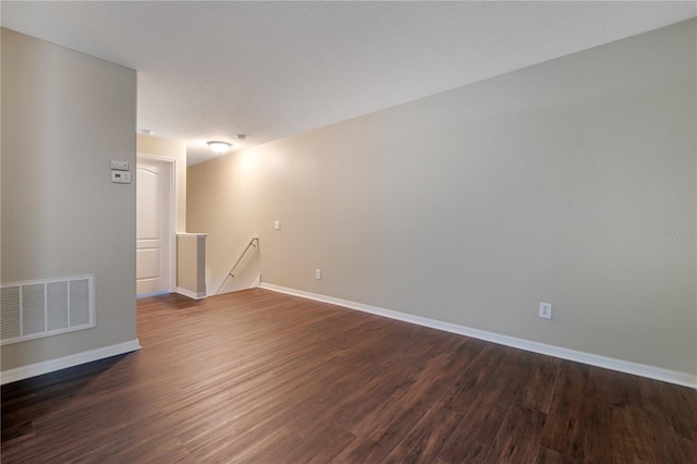 unfurnished room featuring dark wood-style floors, a textured ceiling, visible vents, and baseboards