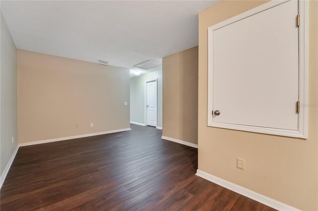 unfurnished room with a textured ceiling, dark wood-type flooring, visible vents, baseboards, and attic access