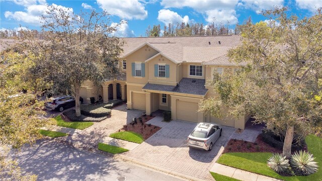 view of front facade with a shingled roof, decorative driveway, an attached garage, and stucco siding