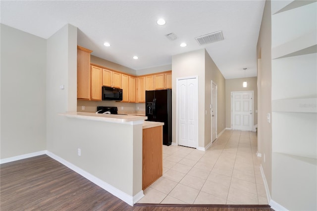 kitchen with visible vents, a peninsula, light countertops, light brown cabinetry, and black appliances