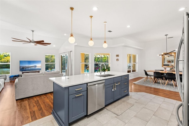 kitchen with light countertops, appliances with stainless steel finishes, open floor plan, a sink, and an island with sink