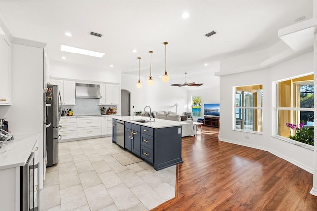 kitchen with open floor plan, decorative light fixtures, wall chimney range hood, white cabinetry, and a sink