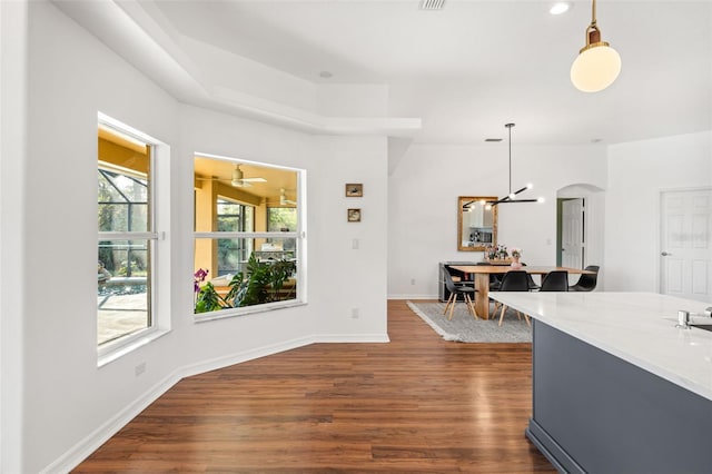 interior space featuring arched walkways, dark wood-type flooring, baseboards, hanging light fixtures, and light stone countertops