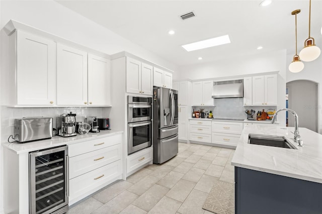 kitchen featuring wine cooler, decorative light fixtures, appliances with stainless steel finishes, a sink, and wall chimney range hood