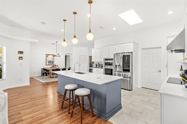 kitchen featuring white cabinets, appliances with stainless steel finishes, light countertops, a large island with sink, and pendant lighting