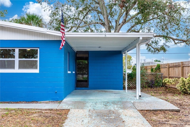 property entrance with driveway, an attached carport, and fence