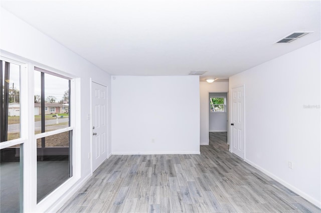 empty room with light wood-type flooring, visible vents, and baseboards