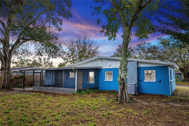 back of property at dusk with a lawn, fence, and a sunroom