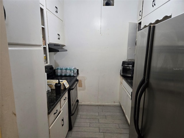 kitchen featuring black / electric stove, under cabinet range hood, white cabinetry, freestanding refrigerator, and dark stone counters