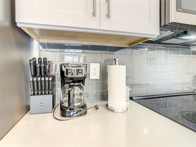 room details featuring light countertops, cooktop, white cabinets, and backsplash