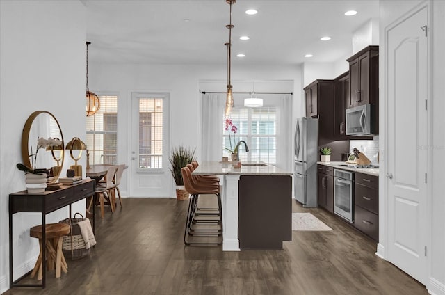 kitchen with decorative light fixtures, appliances with stainless steel finishes, dark wood-type flooring, a sink, and dark brown cabinetry