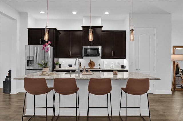 kitchen with a sink, appliances with stainless steel finishes, backsplash, dark wood finished floors, and a center island with sink