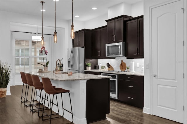 kitchen featuring decorative backsplash, dark wood finished floors, appliances with stainless steel finishes, a kitchen island with sink, and a sink