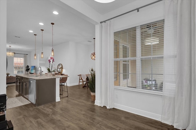 kitchen featuring a breakfast bar area, dark wood-style flooring, stainless steel dishwasher, an island with sink, and pendant lighting