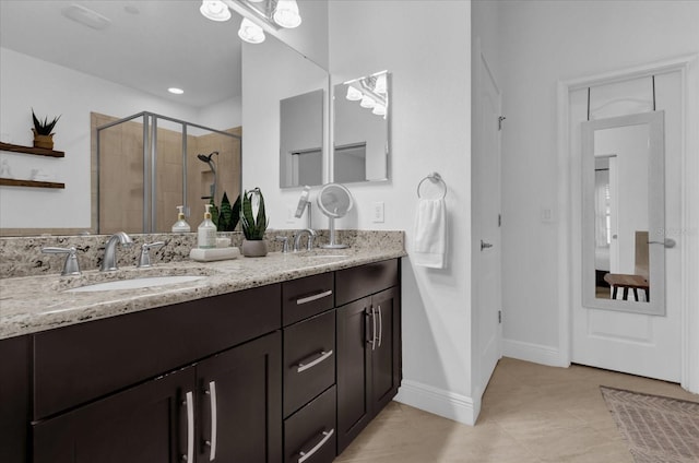 full bathroom with double vanity, a shower stall, baseboards, and a sink