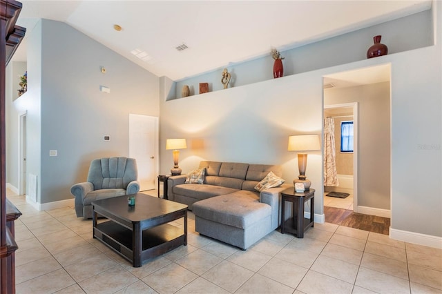 living area featuring light tile patterned floors, high vaulted ceiling, visible vents, and baseboards