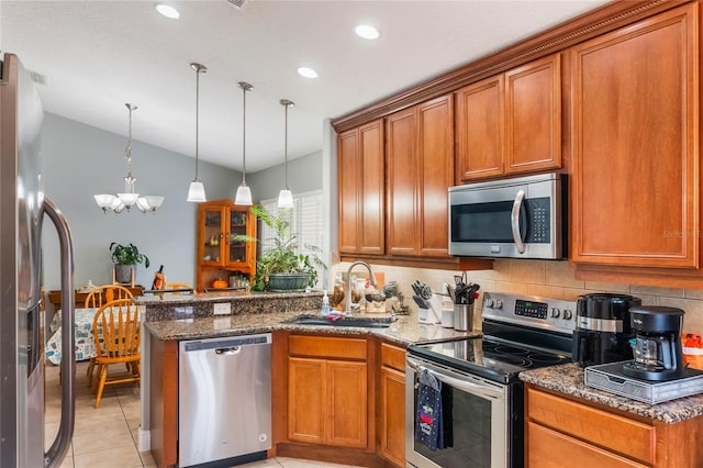 kitchen with appliances with stainless steel finishes, brown cabinetry, a sink, dark stone counters, and a peninsula