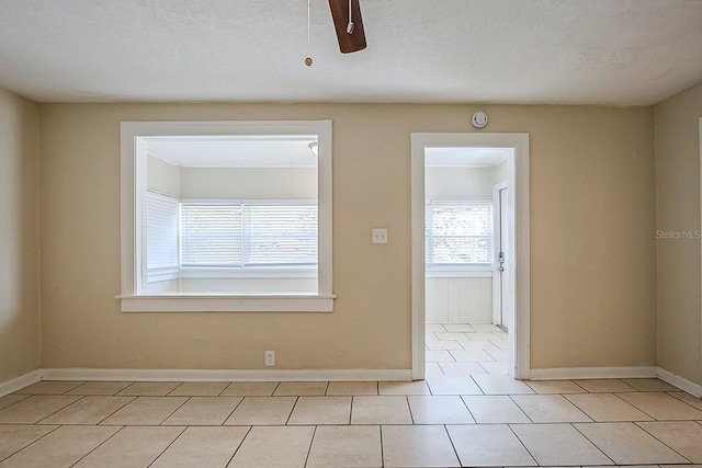 empty room with tile patterned floors, a ceiling fan, baseboards, and a textured ceiling