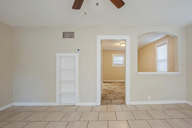 empty room with built in features, a ceiling fan, baseboards, visible vents, and tile patterned floors