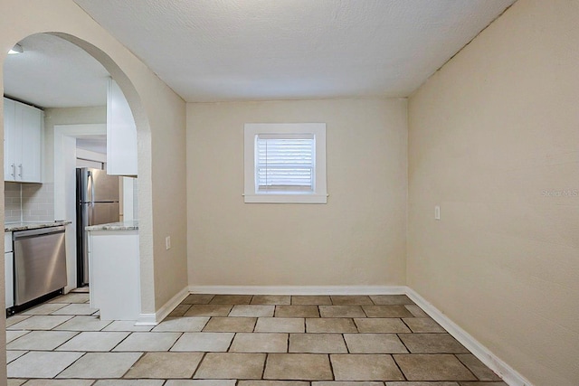 empty room featuring light tile patterned floors, baseboards, arched walkways, and a textured ceiling