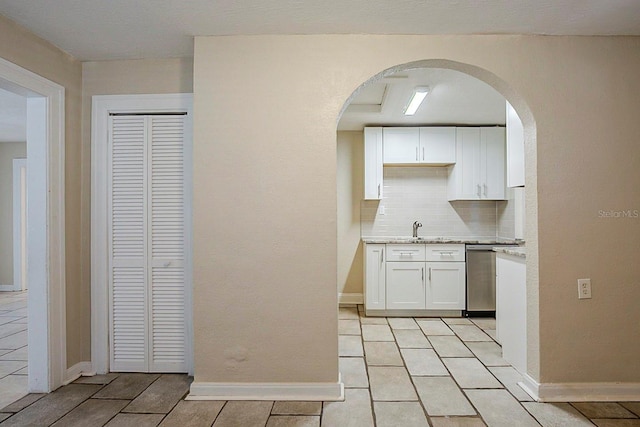 kitchen with a sink, backsplash, stainless steel dishwasher, white cabinetry, and baseboards