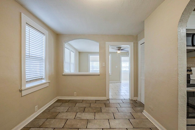 tiled empty room with arched walkways, baseboards, and ceiling fan