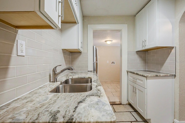 kitchen with light stone counters, light tile patterned floors, a sink, decorative backsplash, and white cabinets