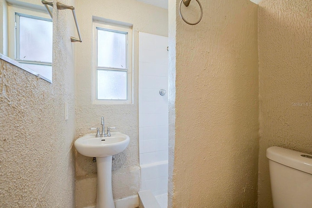 full bathroom featuring a textured wall, toilet, and a tile shower