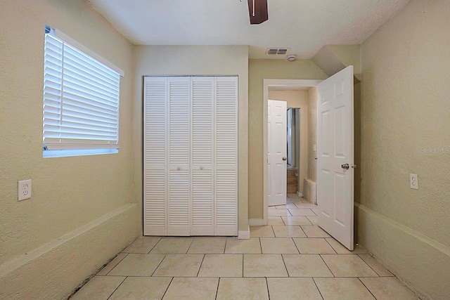 unfurnished bedroom with light tile patterned floors, a ceiling fan, visible vents, a closet, and a textured wall