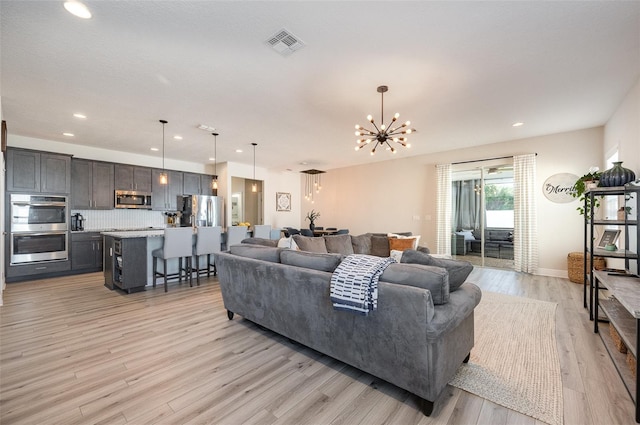 living area with visible vents, baseboards, light wood-style flooring, an inviting chandelier, and recessed lighting