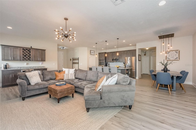 living room with a chandelier, a textured ceiling, recessed lighting, visible vents, and light wood finished floors