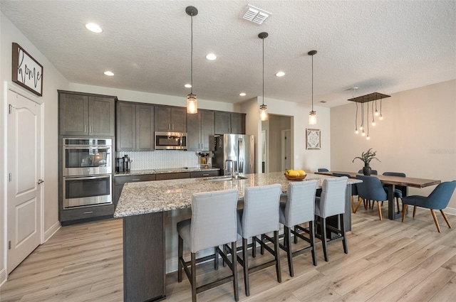 kitchen featuring hanging light fixtures, dark brown cabinetry, a center island with sink, and stainless steel appliances