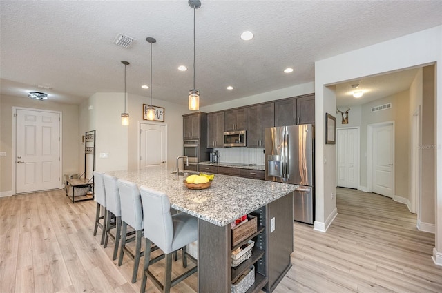 kitchen featuring a center island with sink, visible vents, light stone countertops, stainless steel appliances, and dark brown cabinets