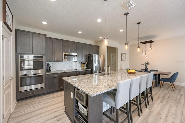 kitchen with a center island with sink, visible vents, stainless steel appliances, pendant lighting, and a sink