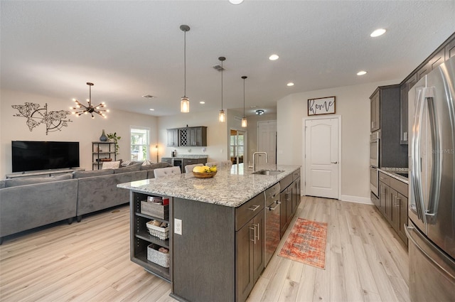 kitchen featuring stainless steel appliances, open floor plan, a kitchen island with sink, a sink, and dark brown cabinets