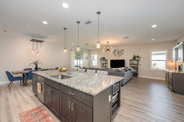 kitchen with dark brown cabinets, a sink, a kitchen island with sink, and light stone countertops