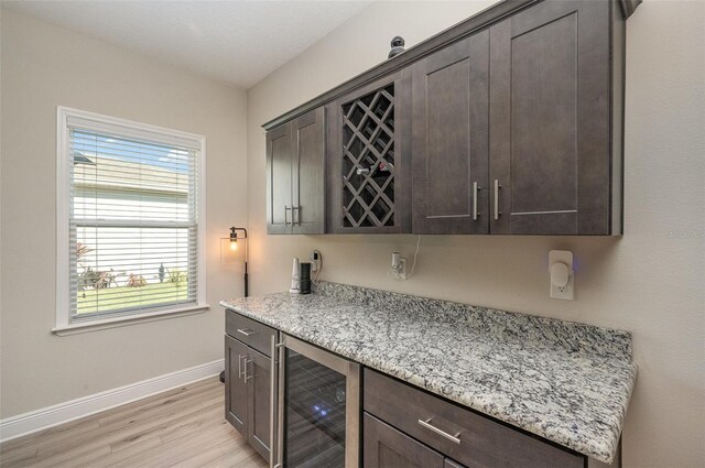 bar with beverage cooler, a dry bar, light wood finished floors, and baseboards